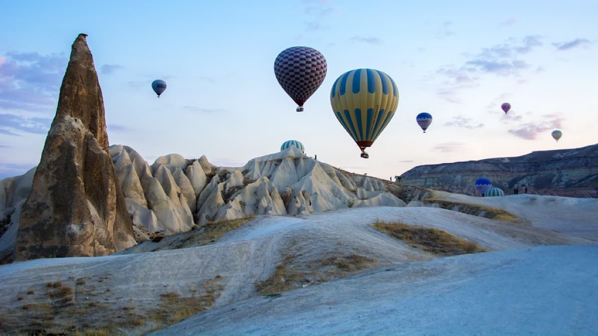 Hot-air balloons drifting over pale rock formations at dawn