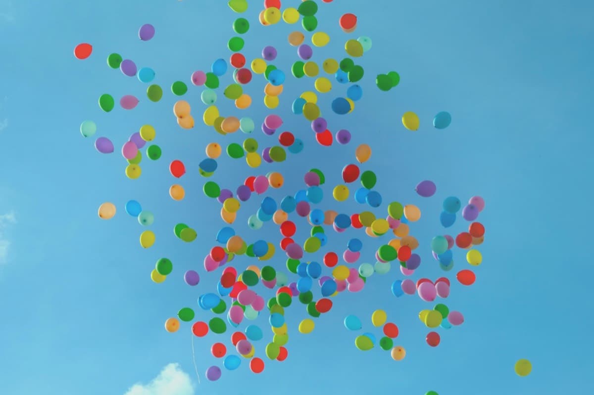 Hundreds of coloured balloons rising together into a clear blue sky
