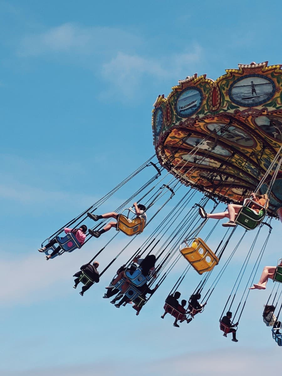 Riders on a painted swing carousel flung out over a clear blue sky, seen from below