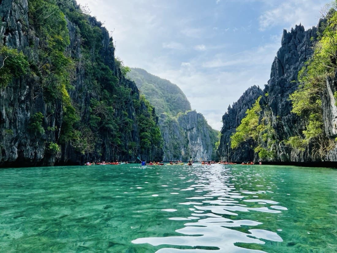Kayakers in red and yellow boats threading a turquoise lagoon between limestone cliffs