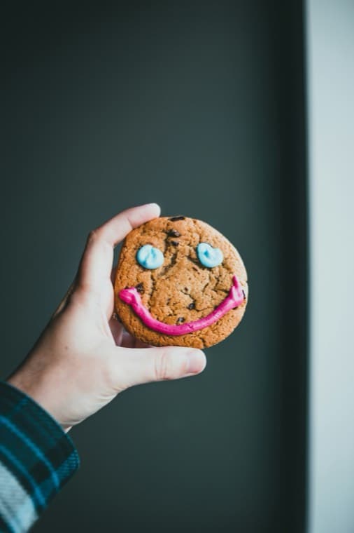 A hand holding a cookie iced with a smiling face