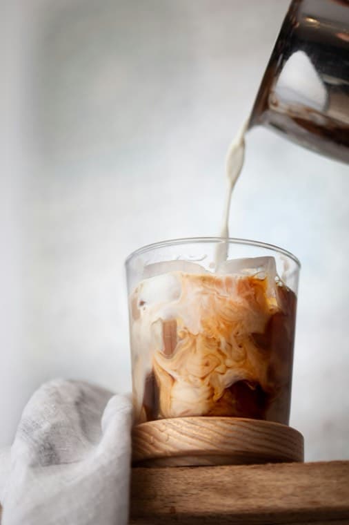 Milk being poured into a glass of iced coffee