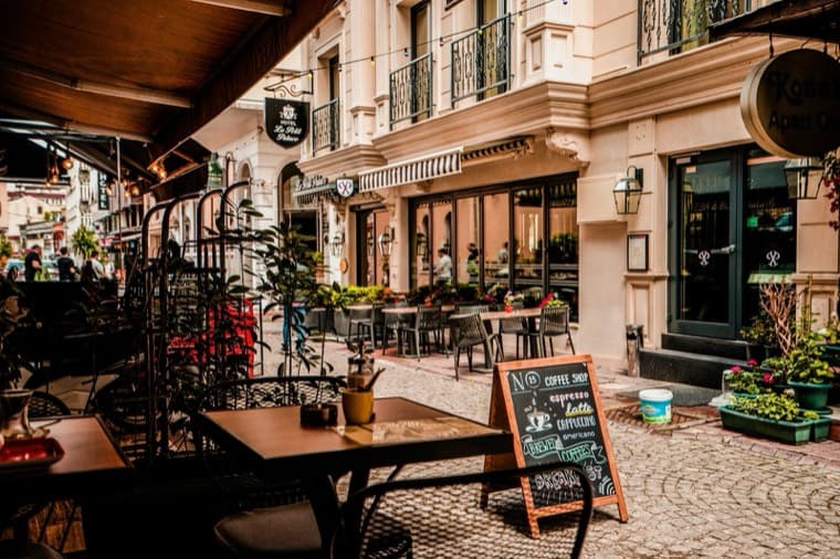 Pavement tables outside a corner coffee shop with a chalkboard menu