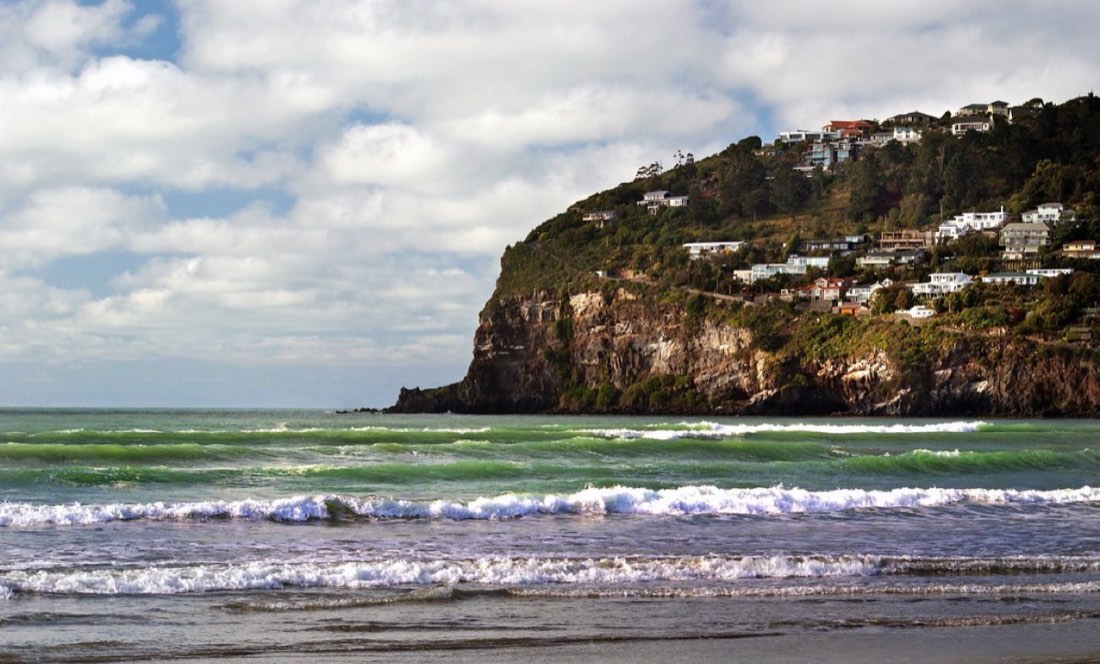 Green surf rolling in below a cliff-top village