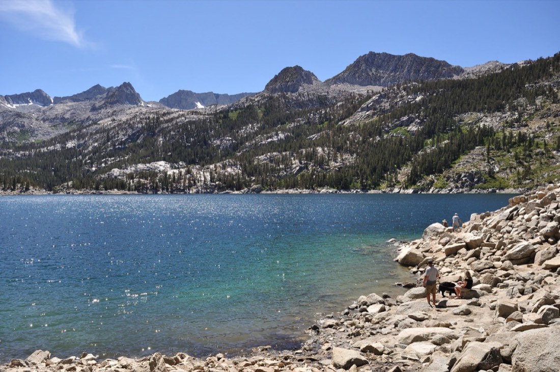 Hikers resting on pale boulders beside a deep blue alpine lake