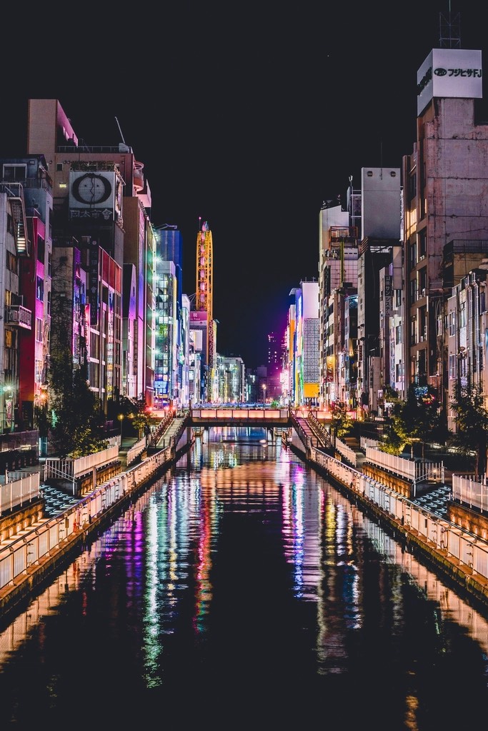 A city canal at night with pink and violet signage reflected the full length of the water
