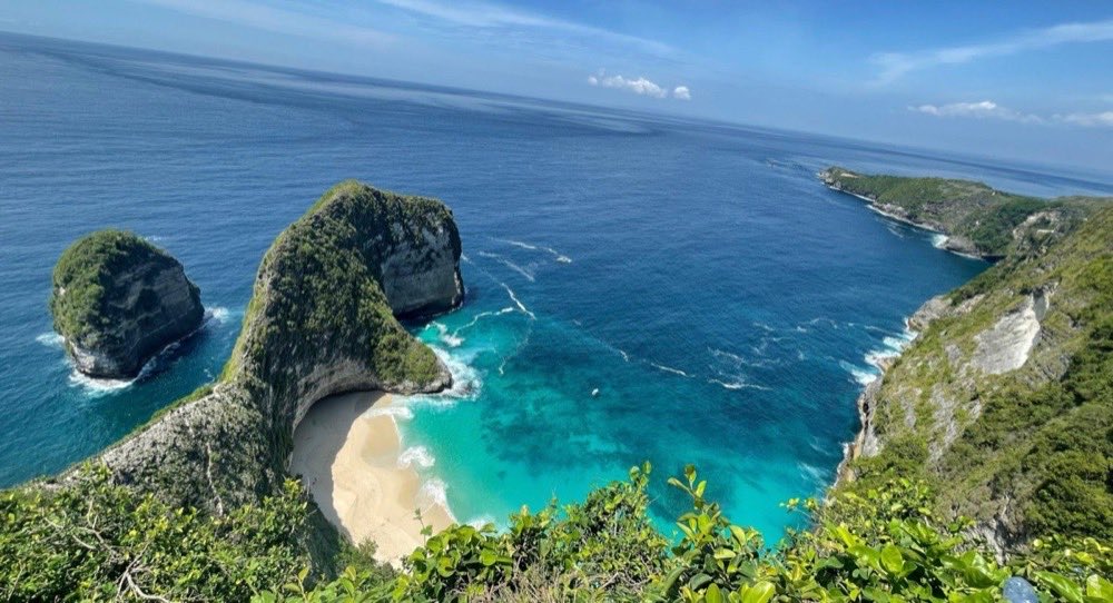 A green headland curving around a white sand cove and bright turquoise shallows