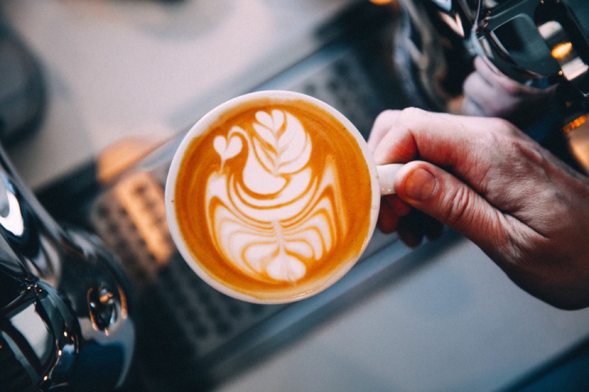 Two hands cupping a flat white with a leaf poured into the crema