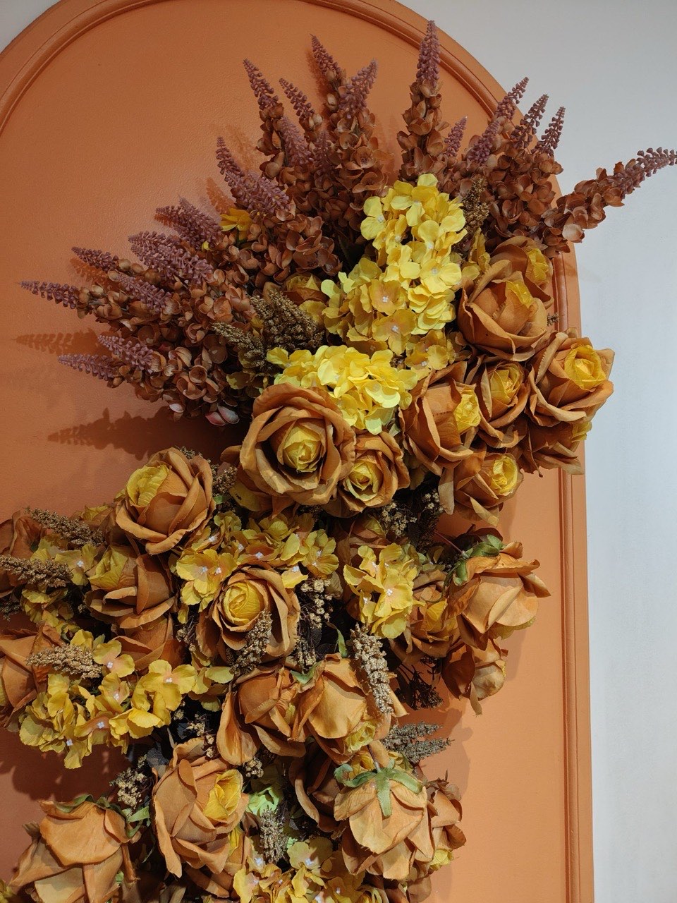A dried arrangement of ochre roses and rust astilbe mounted against a terracotta arch