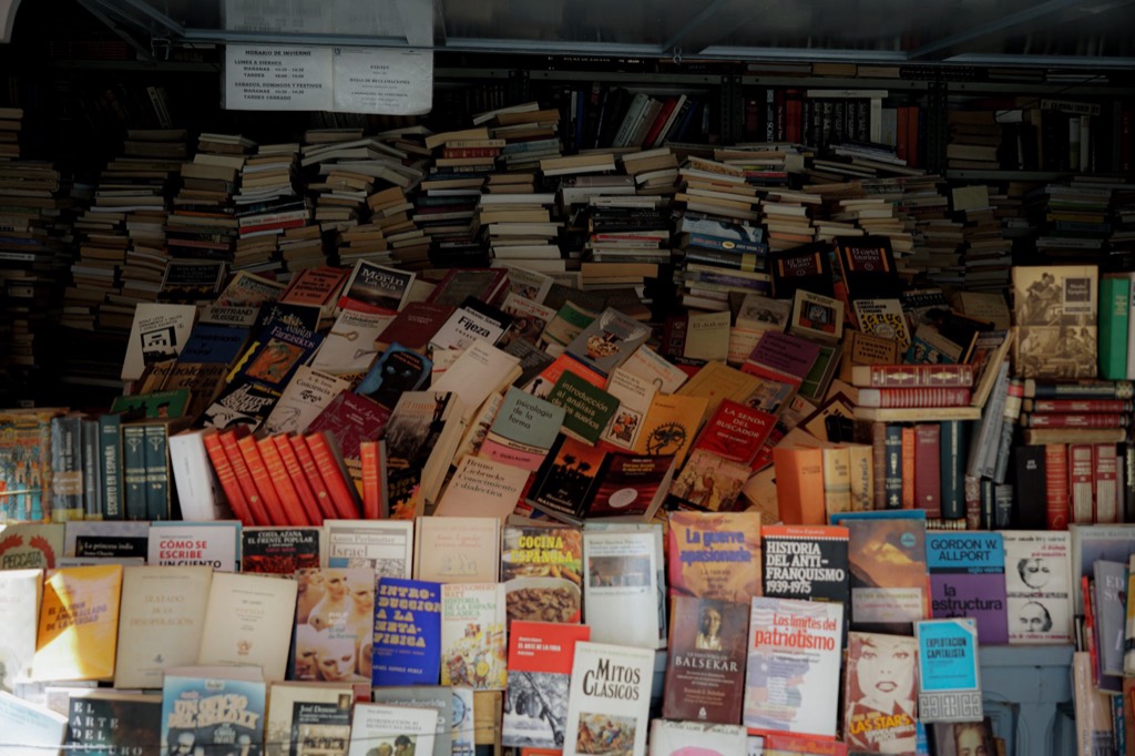 A secondhand book table piled several layers deep with paperbacks, spines facing every direction.