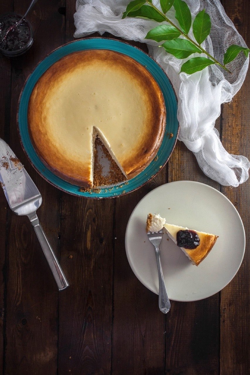 A burnt Basque cheesecake shot from directly above on a teal plate, one wedge cut and moved to a side plate with a fork and berry compote