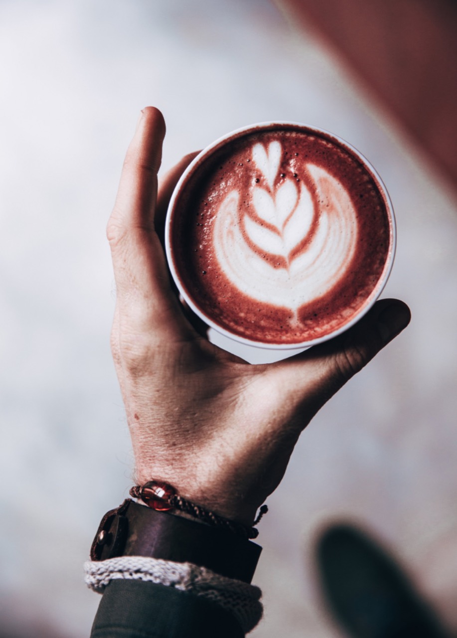A beetroot latte with a tulip poured into it, held up on the flat of one hand and shot from above
