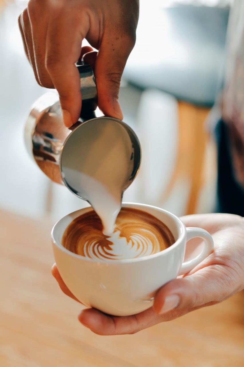 Milk poured from a steel jug into a cup held flat on an open palm, the rosetta half formed