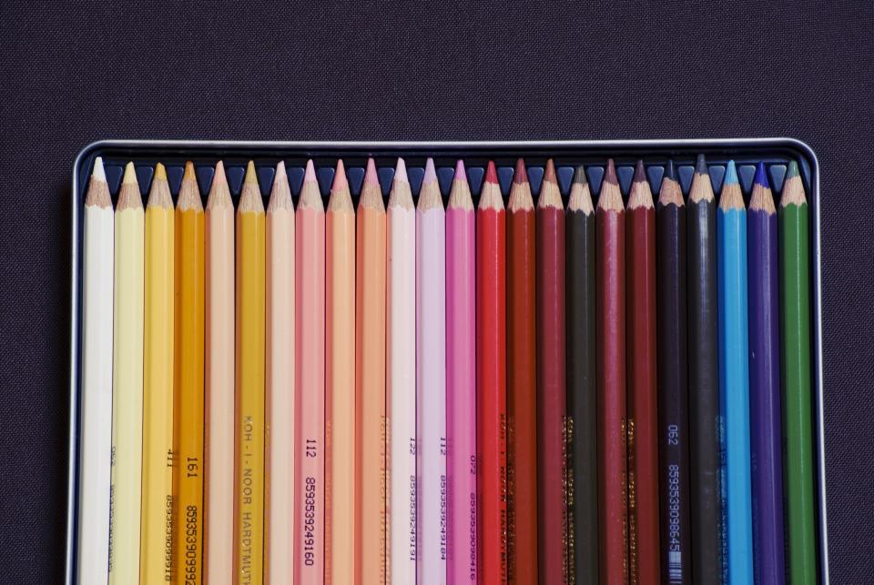 A tin of coloured pencils laid out in a graded row from cream through red to blue.