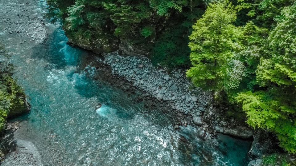 A turquoise river running through a narrow rock gorge with bright green trees over both banks.