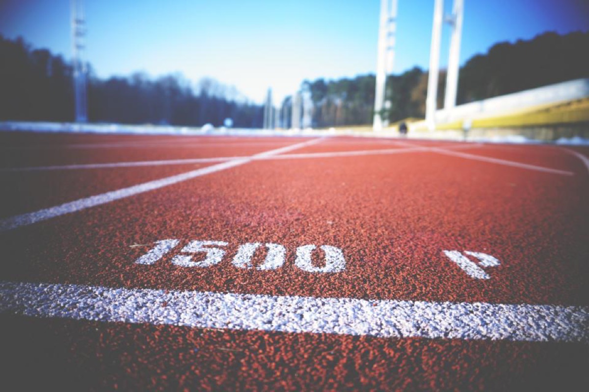 The 1500m start marking painted on a red running track, shot from ground level with the stadium out of focus behind.