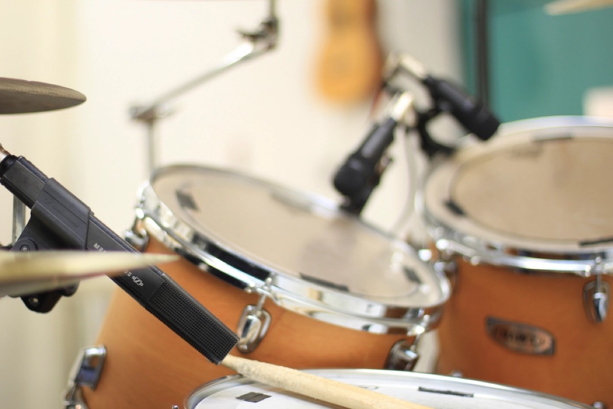 A drum kit photographed close and shallow, a stick resting across the snare and mic stands angled in over the toms