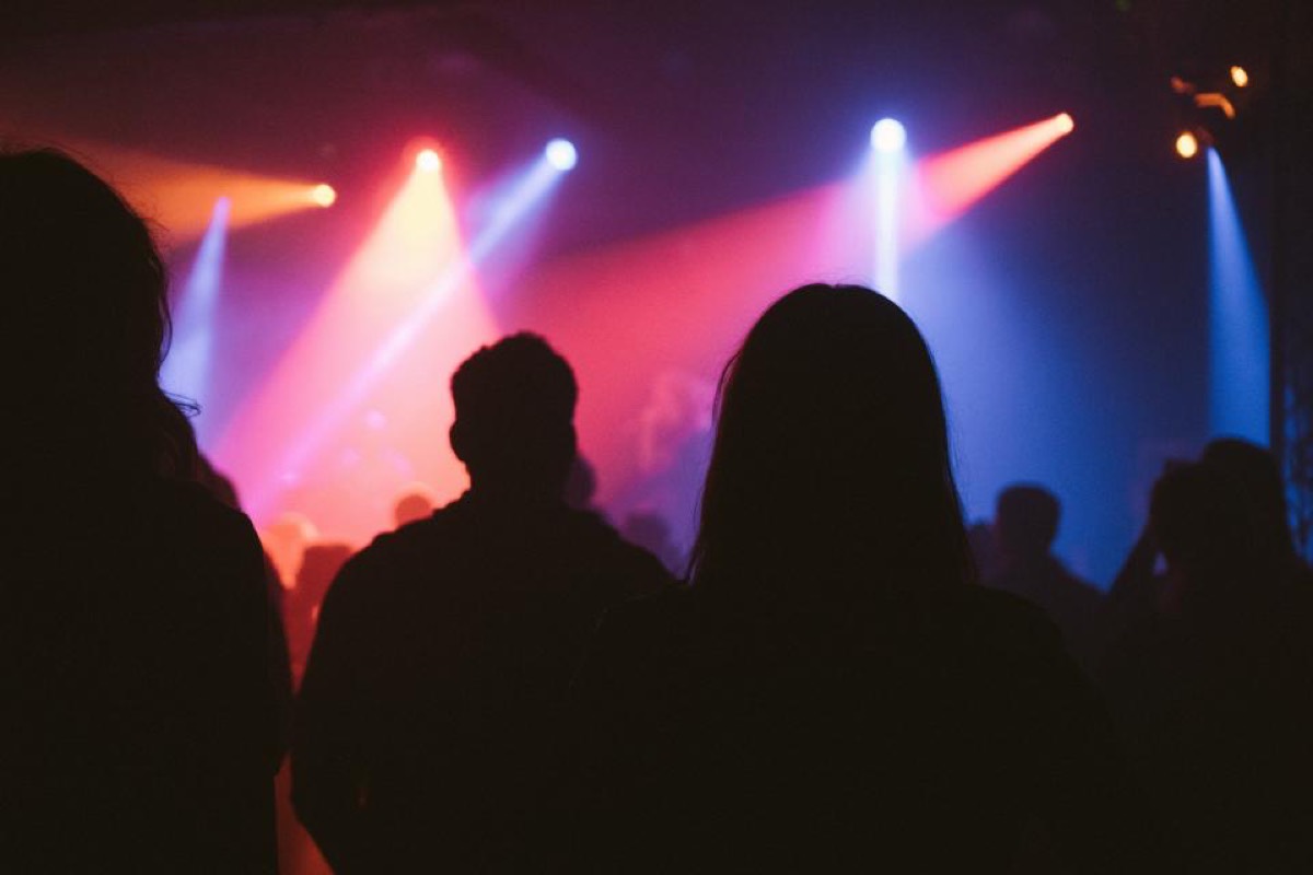 Magenta and blue spotlight beams crossing above a stage with the front row silhouetted in the foreground