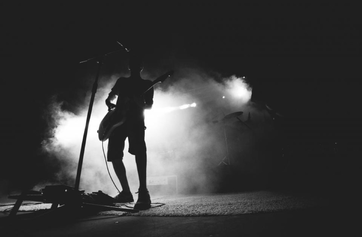 A guitarist in complete silhouette against a wall of backlit smoke, framed by the mic stand, in black and white